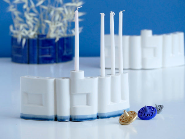 **Innovative “Shalom” Hanukkah Menorah (Chanukiah)**
A unique arc-shaped menorah spelling the Hebrew word *Shalom* (שלום), slip-cast by us in our Tel Aviv studio. Off-white clay, matte off-white glaze, with a subtle blue accent along the base—blending tradition with a fresh, modern look.
