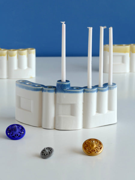 **Innovative “Shalom” Hanukkah Menorah (Chanukiah)**
A unique arc-shaped menorah spelling the Hebrew word *Shalom* (שלום), slip-cast by us in our Tel Aviv studio. Off-white clay, matte off-white glaze, with a subtle blue accent along the base—blending tradition with a fresh, modern look.