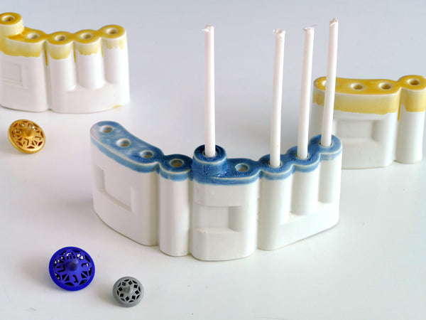 **Innovative “Shalom” Hanukkah Menorah (Chanukiah)**
A unique arc-shaped menorah spelling the Hebrew word *Shalom* (שלום), slip-cast by us in our Tel Aviv studio. Off-white clay, matte off-white glaze, with a subtle blue accent along the base—blending tradition with a fresh, modern look.