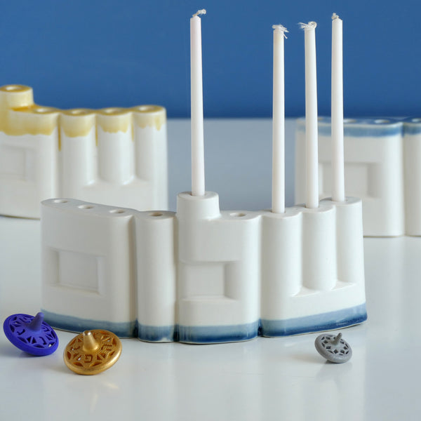 **Innovative “Shalom” Hanukkah Menorah (Chanukiah)**
A unique arc-shaped menorah spelling the Hebrew word *Shalom* (שלום), slip-cast by us in our Tel Aviv studio. Off-white clay, matte off-white glaze, with a subtle blue accent along the base—blending tradition with a fresh, modern look.
