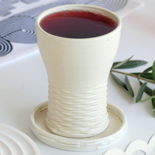 This elegant Kiddush cups set has clean shape with weaving pattern at its bottom - created in a unique method by a clay 3D Printer. The set includes one large Kiddish wine goblet with a plate, and six matching small cups.