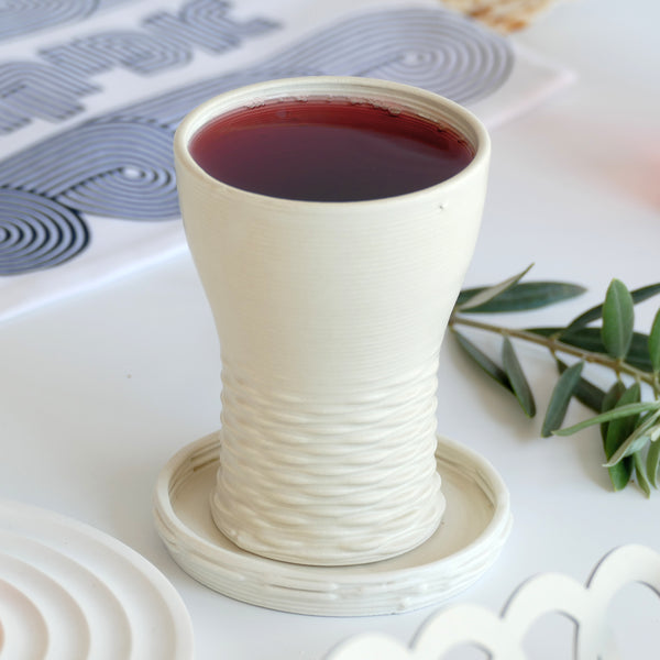 This elegant Kiddush cups set has clean shape with weaving pattern at its bottom - created in a unique method by a clay 3D Printer. The set includes one large Kiddish wine goblet with a plate, and six matching small cups.