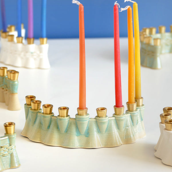 This contemporary Hanukkah Menorah features an arc shape with a delicate weaving pattern, created using a unique method with a clay 3D printer. Its gentle details and modest proportions make it look like a modern jewel.