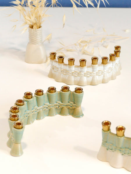 This contemporary Hanukkah Menorah features an arc shape with a delicate weaving pattern, created using a unique method with a clay 3D printer. Its gentle details and modest proportions make it look like a modern jewel.