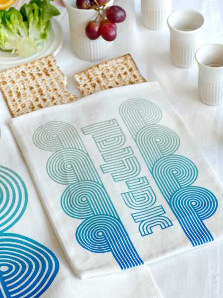 set of a Matzah cover and Afikoman bag, crafted from fine off-white cotton. The design features an op-art-inspired wave pattern in stunning turquoise Ombre tones, printed using state-of-the-art 'Kornit Digital' textile printers. This design draws inspiration from the story of Exodus, merging tradition with contemporary aesthetic.