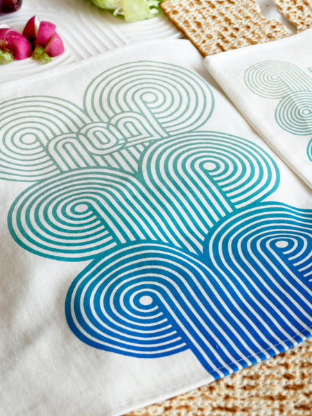 set of a Matzah cover and Afikoman bag, crafted from fine off-white cotton. The design features an op-art-inspired wave pattern in stunning turquoise&nbsp; Ombre tones, printed using state-of-the-art 'Kornit Digital' textile printers. This design draws inspiration from the story of Exodus, merging tradition with contemporary aesthetic.