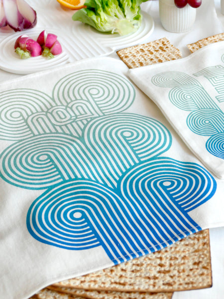 set of a Matzah cover and Afikoman bag, crafted from fine off-white cotton. The design features an op-art-inspired wave pattern in stunning turquoise  Ombre tones, printed using state-of-the-art 'Kornit Digital' textile printers. This design draws inspiration from the story of Exodus, merging tradition with contemporary aesthetic.
